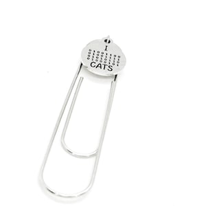 May include: A silver-colored metal paperclip with a circular charm. The charm has the word "I" above a series of binary code and the word "CATS" below. The paperclip is a simple, functional design.