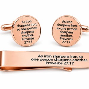 May include: Rose gold cufflinks and tie clip set. The cufflinks are round, and the tie clip is rectangular. Each piece features the text "As iron sharpens iron, so one person sharpens another. Proverbs 27:17."