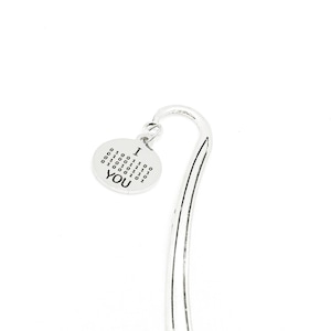 May include: A silver-colored bookmark with a curved top and a circular charm. The charm has the words "I YOU" and binary code. The bookmark is designed to be inserted into a book.