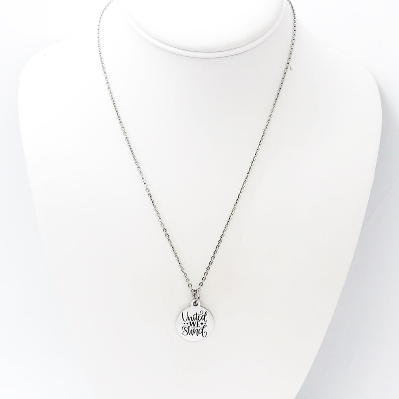 May include: Silver necklace with a round pendant that says "United We Stand" in a cursive font.