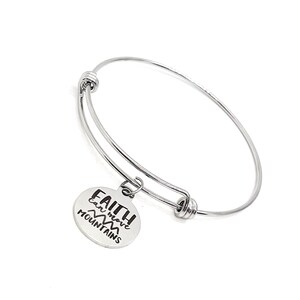 Puede incluir: Un brazalete expandible de plata con un dije redondo que dice "FAITH can move MOUNTAINS".