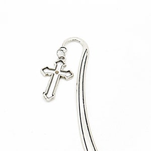May include: Silver metal bookmark with a cross charm. The cross has a detailed design and a small, round, gold-coloured accent in the centre.