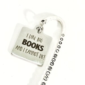 May include: A silver-colored bookmark with the text "I LIKE BIG BOOKS AND I CANNOT LIE!" on a square tag. The bookmark has a curved top and a decorative, patterned stem.