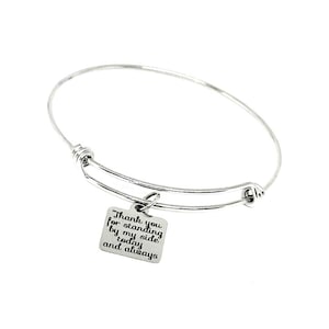 May include: A silver-colored bangle bracelet with a square charm. The charm is engraved with the words "Thank you for standing by my side today and always" in black lettering. The bracelet is on a white background.