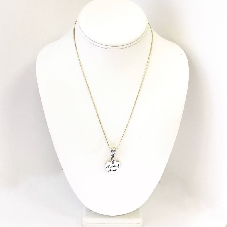 Puede incluir: Un collar de plata con un colgante en forma de coraz&oacute;n que dice "Maid of Honor".