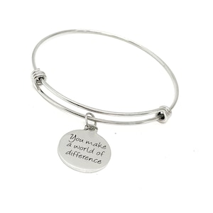 May include: Silver bangle bracelet with a round charm that reads "You make a world of difference".