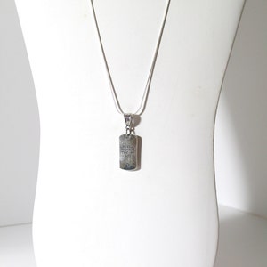 May include: A silver chain necklace with a silver pendant. The pendant is rectangular and has the words "Be still and know that I am God" engraved on it.