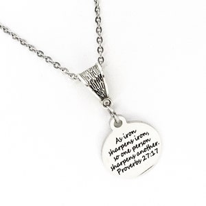 May include: A silver necklace with a round pendant that says "As iron sharpens iron, so one person sharpens another. Proverbs 27:17"