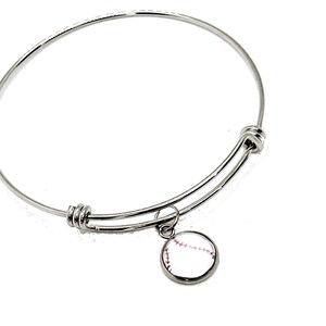 May include: A silver expandable bangle bracelet with a charm of a white baseball with red stitching.