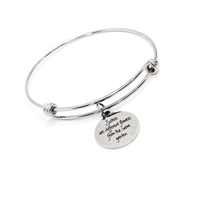 Puede incluir: Un brazalete de plata con un dije que dice "Las hermanas son flores diferentes del mismo jardín".
