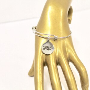 Peut inclure: Bracelet en argent avec un charme rond qui dit "Perfectly Imperfect".
