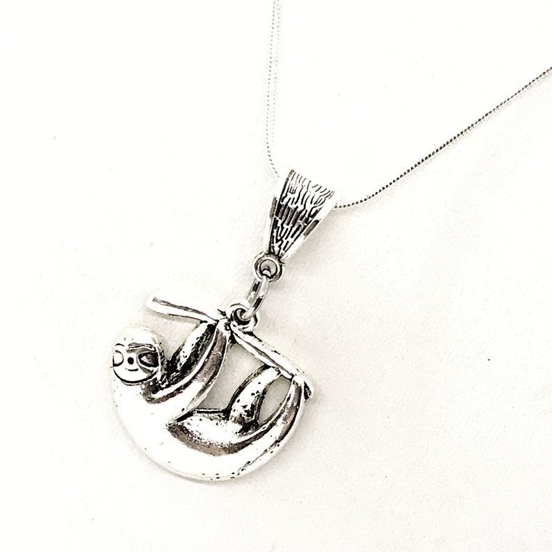 May include: A silver necklace with a sloth pendant. The sloth is hanging from a branch and has a detailed design.