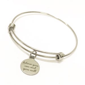 May include: Silver bangle bracelet with a charm that reads "believe you can and you will".
