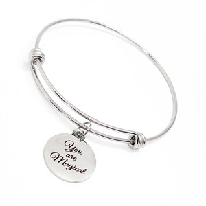 May include: Silver bangle bracelet with a round charm that reads "You are Magical".