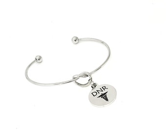 May include: A silver bangle bracelet with a knot detail and a round charm that says "DNR" with a medical symbol.