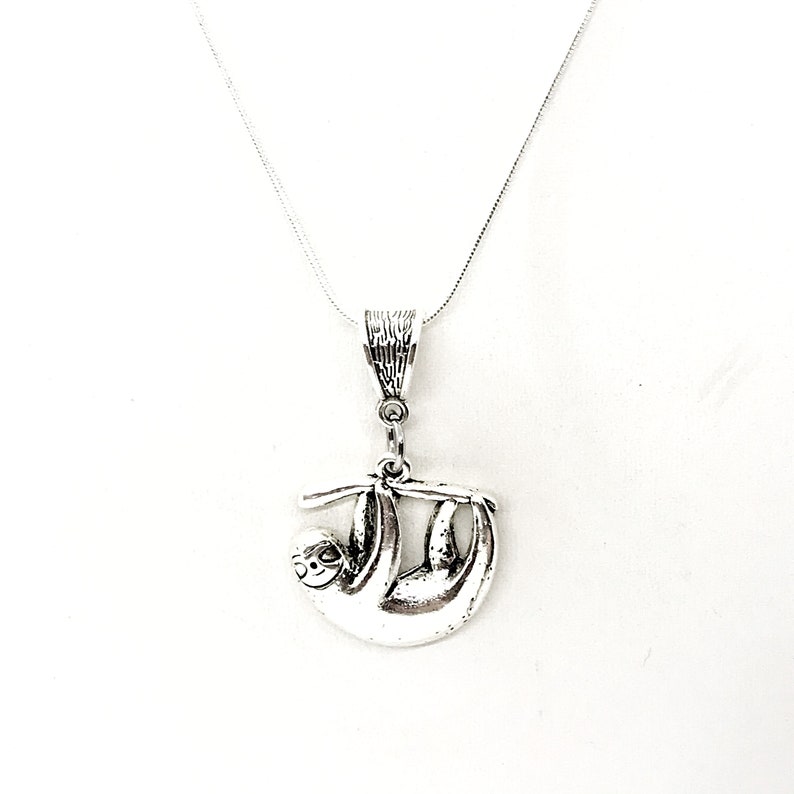 May include: Silver necklace with a sloth pendant. The sloth is hanging upside down from a branch.