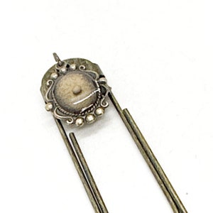 May include: Silver bookmark with a round, ornate, silver charm with a white stone in the center.