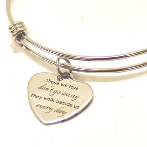 May include: A silver expandable bracelet with a heart-shaped charm that reads "Those we love don't go away, they walk beside us every day."