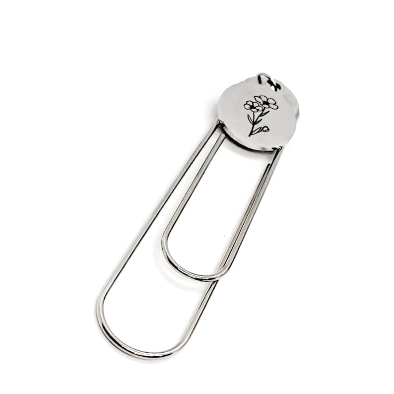 May include: Silver bookmark with a flower design on a round charm. The bookmark is made of metal and has a simple, elegant design.