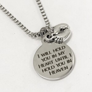 May include: Silver necklace with a round pendant that reads "I will hold you in my heart until I hold you in heaven". The pendant is attached to a silver chain and has a small charm of two baby footprints.