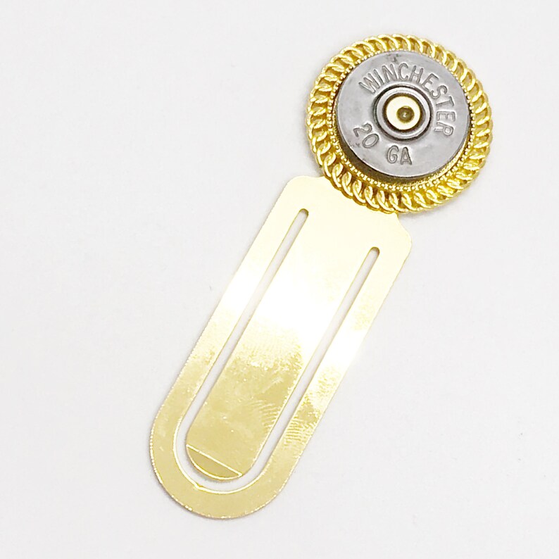 May include: Gold bookmark with a 20 GA Winchester shotgun shell attached to the top. The shell is silver with black lettering.