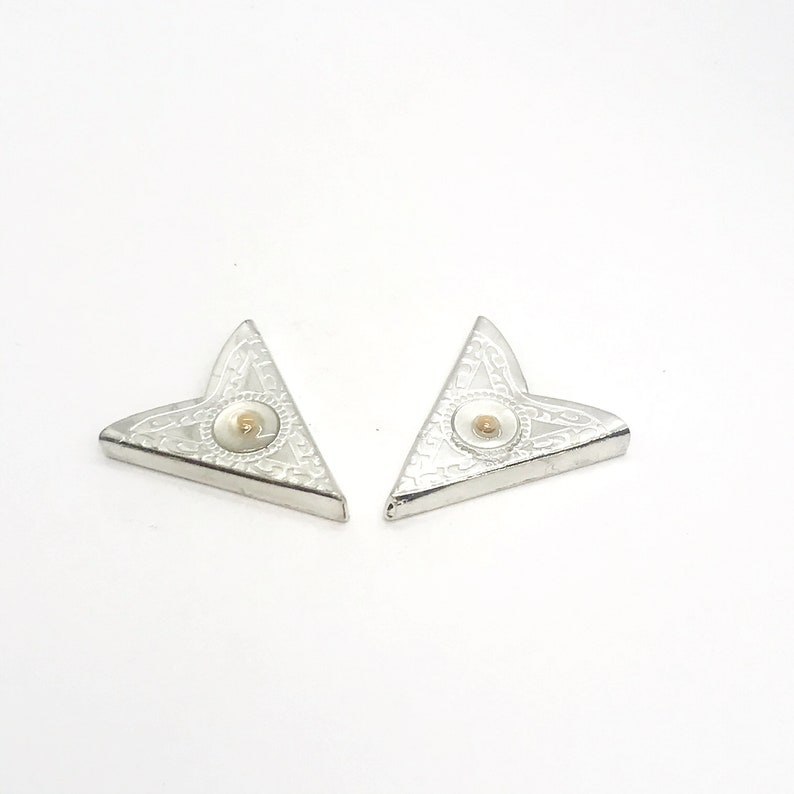 May include: Two silver corner protectors with a decorative design and a gold center. The corner protectors are triangular in shape.