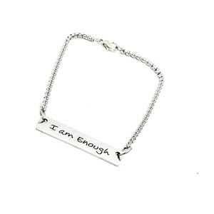 May include: A silver chain bracelet with a silver bar charm that says "I am enough" in handwritten script.