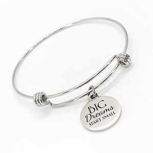 May include: Silver bangle bracelet with a round charm that says "BIG DREAMS START SMALL".