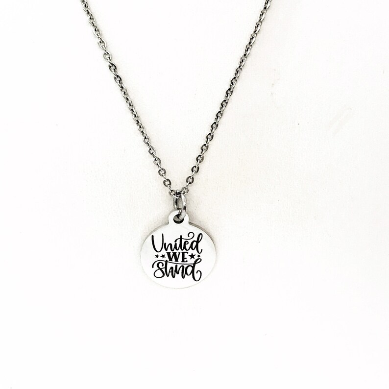 May include: A silver necklace with a round pendant that says "United We Stand" in black lettering.