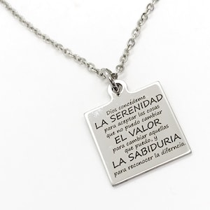 May include: Silver necklace with a square pendant that has an inspirational quote in Spanish engraved on it. The quote reads: "Dios concédeme la serenidad para aceptar las cosas que no puedo cambiar, el valor para cambiar aquellas que puedo, y la sabiduría para reconocer la diferencia."