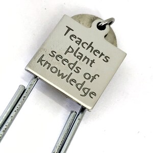 May include: Silver bookmark with a square tag that reads "Teachers plant seeds of knowledge".