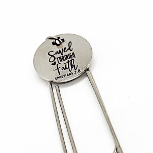 May include: Silver bookmark with a round metal charm that says "Saved Through Faith Ephesians 2:8".