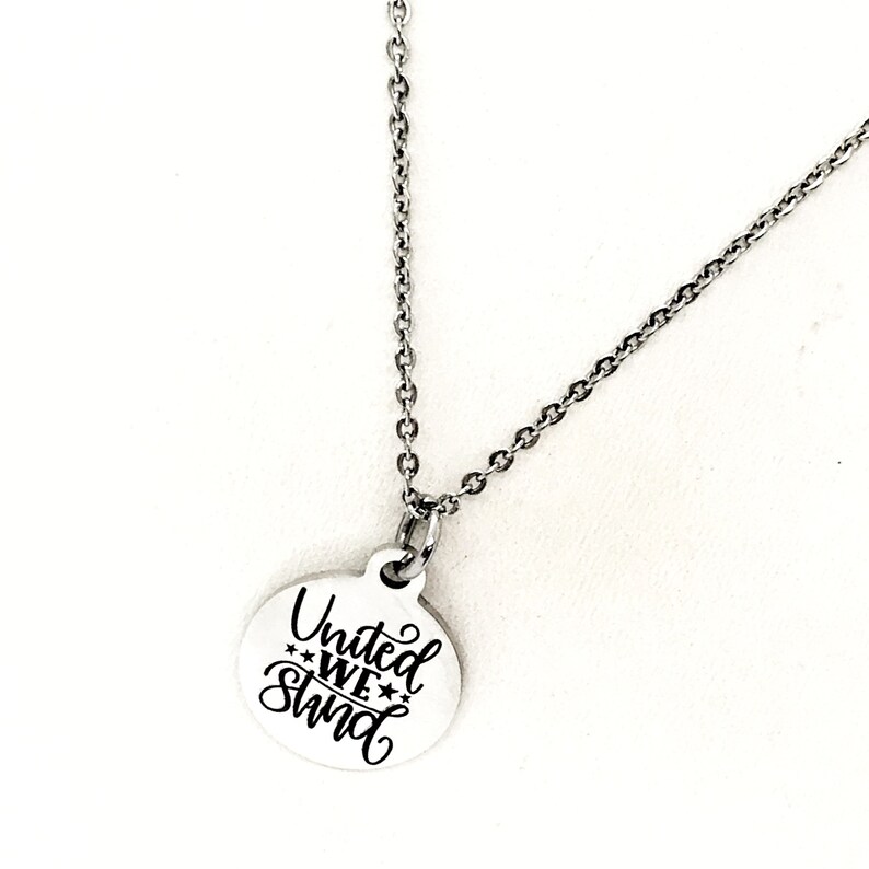 May include: A silver necklace with a round pendant that says "United We Stand" in a cursive font with stars.
