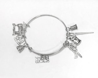 Op de afbeelding: Zilveren armband met bedels met een naai-thema, waaronder een naaimachine, een spoel garen, een vingerhoed, een schaar en een bedel met de tekst "Ik hou van naaien".