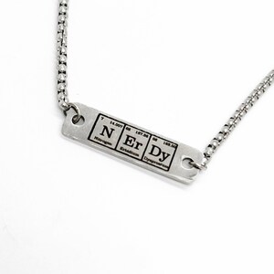 May include: A silver necklace with a rectangular pendant featuring the chemical symbols for nitrogen, erbium, and dysprosium, along with their atomic numbers and weights.
