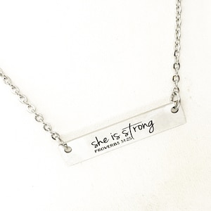 May include: Silver necklace with a bar pendant that reads "she is strong PROVERBS 31:25".