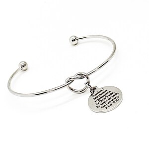 May include: Silver bangle bracelet with a knot charm and a round charm with the text "Therefore, I take pleasure in persecutions for Christ's sake, for when I am weak, then I am strong 2 Cor. 12:10".