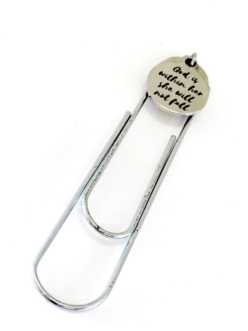 May include: A silver paperclip bookmark with a round charm attached. The charm has the words "God is within her she will not fall" engraved on it.