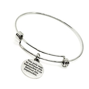 May include: Silver expandable bangle bracelet with a round charm that reads "The only way to achieve the impossible is to believe the impossible."