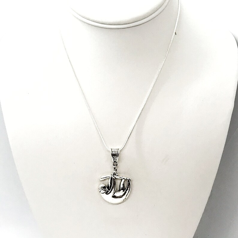 May include: A silver necklace with a sloth pendant. The sloth is hanging upside down from a branch.