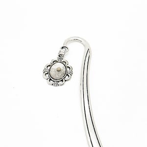 May include: Silver bookmark with a decorative oval charm featuring a floral design. The bookmark is curved and has a silver finish.