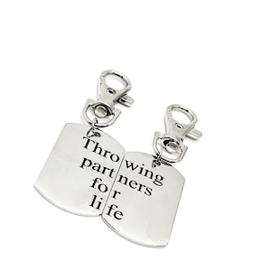 Puede incluir: Dos llaveros plateados con un anillo partido y una etiqueta rectangular. La etiqueta de la izquierda dice "Throwing partners for life". La etiqueta de la derecha dice "Throwing partners for life".