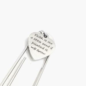 May include: Silver heart-shaped bookmark with the inscription "Faith is like a little seed if planted it will grow".