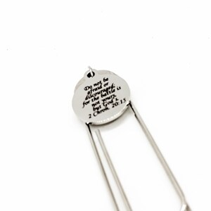 May include: Silver bookmark with a round charm that reads "Do not be afraid or discouraged for the battle is not yours but God's 2 Chron. 20:15".