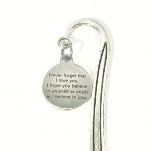 May include: Silver-toned metal bookmark with a curved top and a circular charm. The charm is engraved with the message: "Never forget that I love you. I hope you believe in yourself as much as I believe in you."