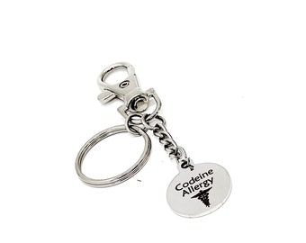 May include: Silver keyring with a round tag that says "Codeine Allergy" with a medical symbol. The keyring has a split ring and a lobster clasp.