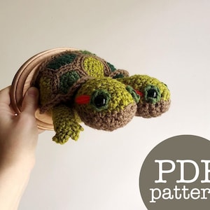 Könnte beinhalten: Häkelanleitung für eine zweiköpfige Schildkröten-Amigurumi. Das Muster ist als PDF-Download erhältlich. Das Bild zeigt eine fertige gehäkelte Schildkröte mit grünem und braunem Garn, zwei Köpfen und einem Panzer.