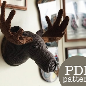 May include: Crocheted moose head wall decor with brown antlers. The moose head is a dark brown color and is mounted on a wooden plaque. The text "PDF pattern" is visible in the lower right corner of the image.