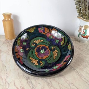 May include: A black ceramic bowl with a floral design. The bowl features a swirling pattern of green leaves, orange and purple flowers, and gold dots on a black background.