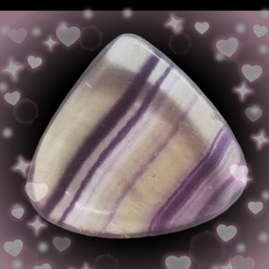 May include: A polished, triangular-shaped fluorite gemstone featuring distinct, parallel bands of translucent white, pale yellow, and deep purple hues. The stone has a smooth, rounded surface with a glossy finish, showcasing natural mineral layering.